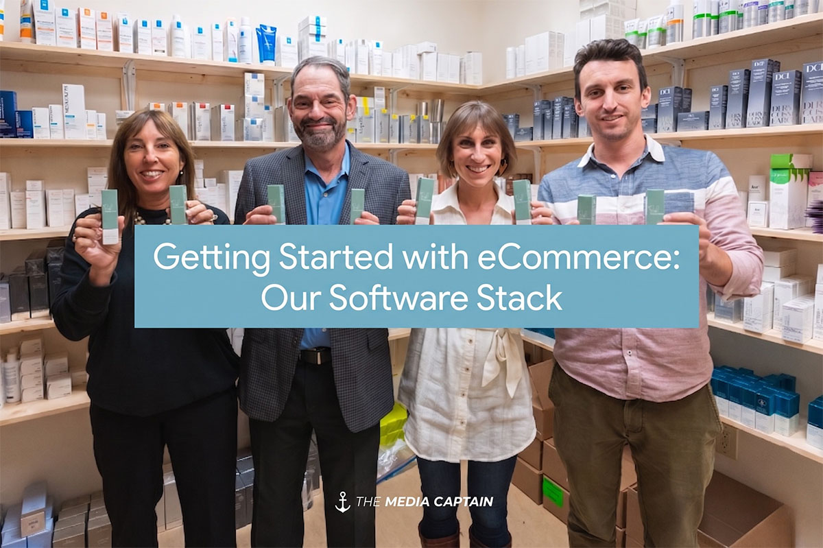 A group of four smiling people stand in a pharmacy or cosmetics store, each holding up small green product boxes for the camera against a background of stocked wooden shelves, with the white text overlay, 'Getting Started with eCommerce: Our Software Stack' centered over them, and a white anchor logo and 'THE MEDIA CAPTAIN' in the bottom center.